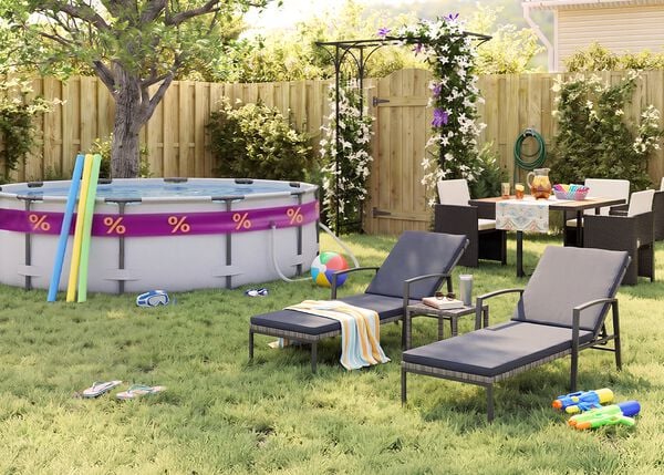 Sonniger Garten hinter dem Haus mit Aufstellpool, Poolnudeln, Schwimmbrille, Wasserball und Flip-Flops im Gras. Zwei schwarze Metall-Sonnenliegen mit grauen Polstern stehen neben einem kleinen Beistelltisch, w&auml;hrend eine Outdoor-Essgruppe mit dunklen Geflechtst&uuml;hlen bei einer bl&uuml;henden Pergola, einem Holzzaun und sommerlichen Gartenaccessoires platziert ist.