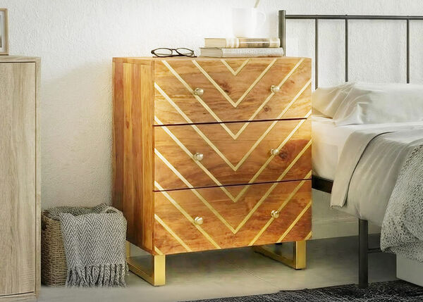 Holz-Nachttisch mit drei Schubladen und geometrischem Goldmuster neben einem Bett in einem hellen Schlafzimmer.