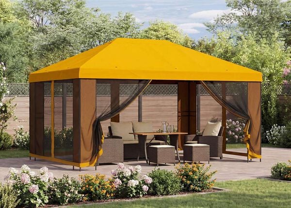 Gelber Gartenpavillon mit Netzvorh&auml;ngen, der eine Sitzgruppe mit Tisch auf einer Terrasse in einem sonnigen Garten mit bl&uuml;henden Pflanzen &uuml;berdacht.