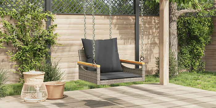 Rattan-Schaukelbank für draußen mit dunklen Kissen auf einer Terrasse. Klick drauf, um die Kollektion zu shoppen.
